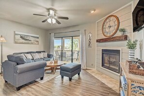 A living room with a sofa, ottoman, fireplace, and a ceiling fan. - Dog-friendly Water View Condo With Inviting Porch, AC, W/d, & Modern Charm (Horseshoe Bay)