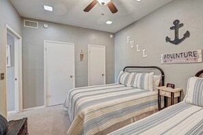 A bedroom with two beds, a ceiling fan, a wall clock, and a sign that says 'ADVENTURE awaits.' - Dog-friendly Water View Condo With Inviting Porch, AC, W/d, & Modern Charm (Horseshoe Bay)