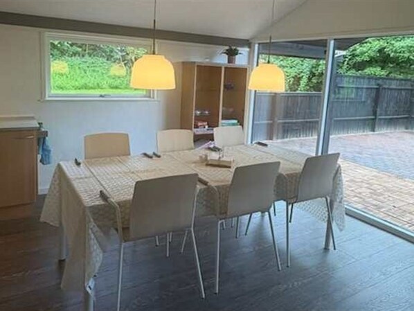 Een eetruimte met een tafel, stoelen, hanglampen en uitzicht op het buiten.
