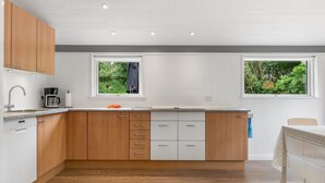 Une cuisine moderne avec des meubles en bois, un lave-vaisselle encastré et deux fenêtres donnant sur un paysage verdoyant.