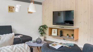 Un salon moderne doté d’un téléviseur à écran plat, de canapés gris, d’une petite table ronde et d’un lambris en bois.
