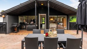 Un espace extérieur moderne aménagé pour les repas, avec une table et des chaises, un barbecue et une terrasse couverte.