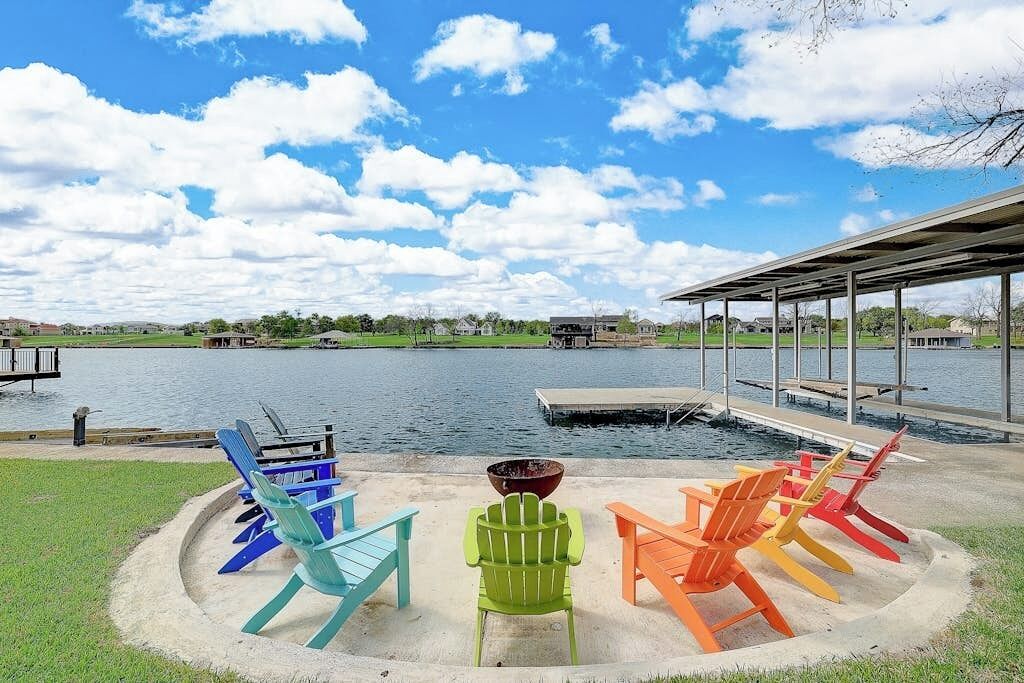 Terraza junto al lago con sillas Adirondack de colores, un hogar para fogata y un área de estar cubierta.