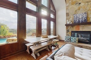 Una habitación con chimenea de piedra, una mesa de madera con bancos y vista a una piscina, junto con un ventanal grande.