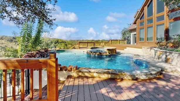 Une piscine dotée d’une terrasse en bois, d’une structure en pierre et d’un bâtiment avec de grandes fenêtres.
