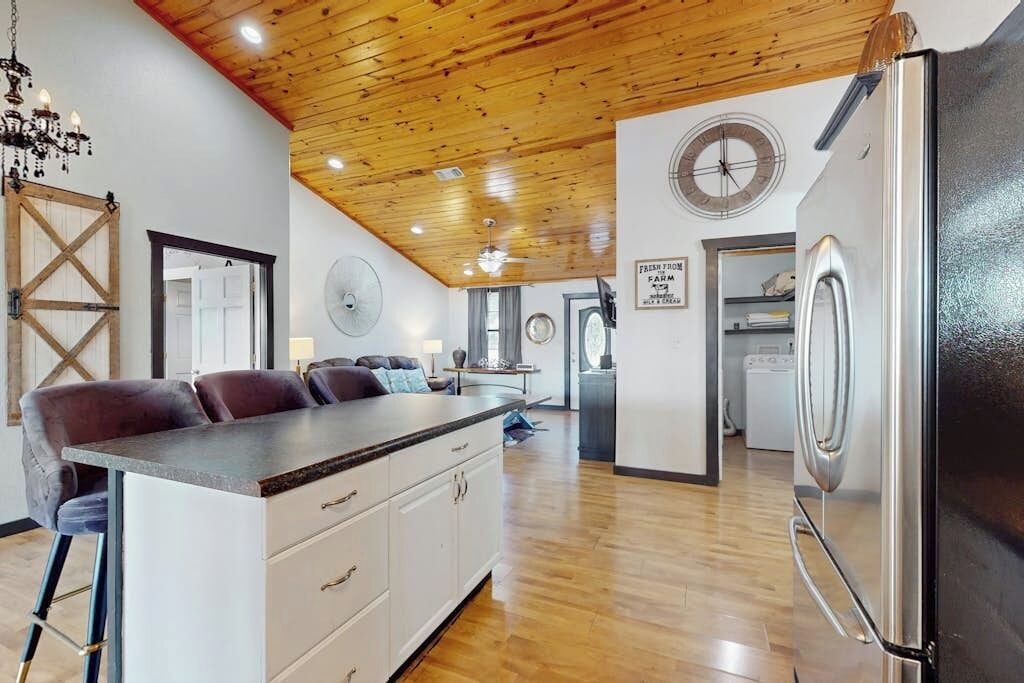Een moderne keuken met een centraal eiland, houten plafond en een koelkast.
