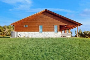 Ein zweistöckiges Holzhaus mit Steinfundament, einer Veranda und einem grünen Rasen.
