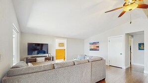 Una sala de estar con sofá, televisión, ventilador de techo y obras de arte en las paredes.