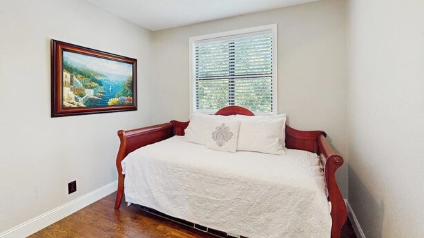 Un dormitorio con cama, ventilador de techo, ventana con persianas y un cuadro en la pared.