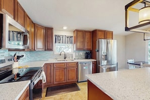 A modern kitchen with wooden cabinets, stainless steel appliances, a granite countertop, and a window with curtains. - Waterfront House on Lake LBJ With Full Kitchen, Patio, Pool Table & Dog-friendly (Marble Falls)