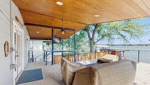 Un patio al aire libre con zona de estar cubierta, techo de madera y vistas a un lago.