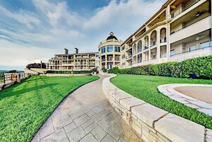 Un hotel grande de varios pisos con un patio central, un camino curvo y un césped bien cuidado.