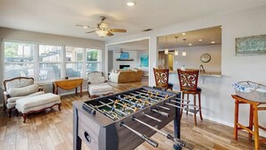 A spacious living room with a foosball table, comfortable seating, and large windows.