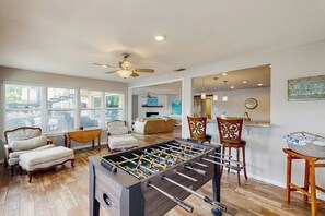A spacious living room with a foosball table, comfortable seating, and large windows.