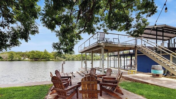 A lakeside deck with Adirondack chairs, a covered seating area, and a dock extending into the water.
