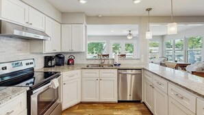 A modern kitchen with white cabinets, stainless steel appliances, and a large window providing a view of the outdoors.
