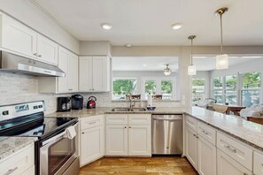 A modern kitchen with white cabinets, stainless steel appliances, and a large window providing a view of the outdoors.