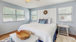 Um quarto com cama, ventoinha no teto, grinalda na parede e mesa de cabeceira com abajur.