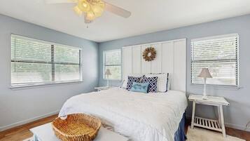 A bedroom with a bed, a ceiling fan, a wall-mounted wreath, and a bedside table with a lamp.