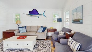 Sala de estar com sofá, mesa de centro, tapete estampado e obras de arte na parede, incluindo um peixe e um veleiro.