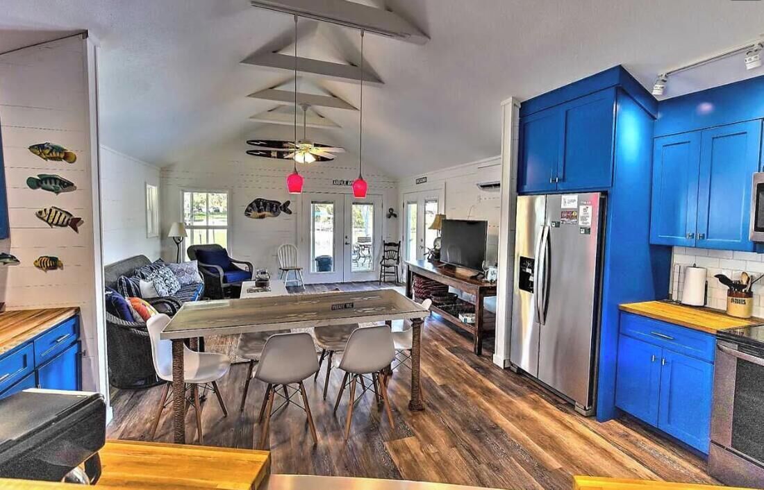 A modern kitchen with blue cabinets, a central island with chairs, and a dining area with a wooden table.
