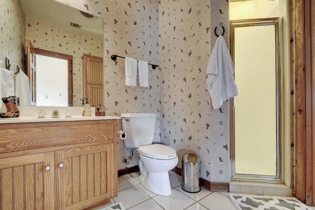 A bathroom with a wooden vanity, a toilet, a shower area, and a mirror.