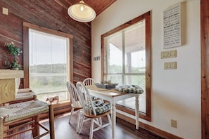 A rustic dining area with wooden walls, large windows, a table with chairs, and a wall-mounted light fixture. - Regal Riverfront Home With 2 Cabins - 2 Miles to Marina (Spicewood)