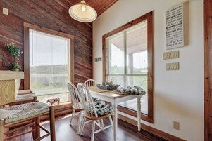 Un comedor rústico con paredes de madera, ventanas amplias, una mesa con sillas y una lámpara fijada a la pared.