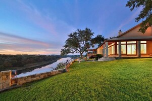 Una casa con vista al río, paredes de piedra y un césped.
