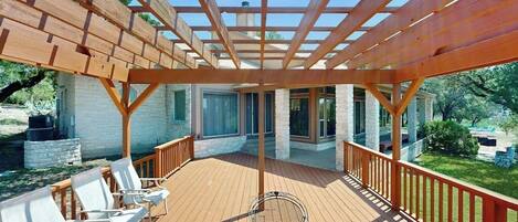 A covered outdoor deck with wooden railings, a glass table, and white chairs.