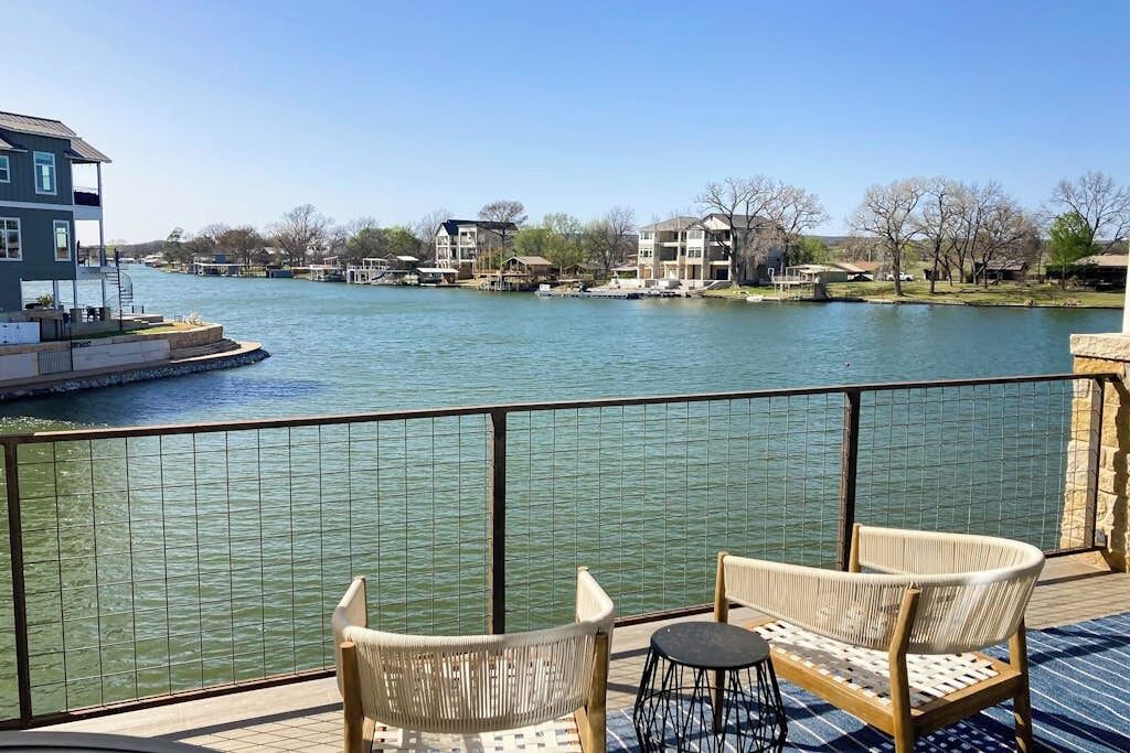 Eine Terrasse mit Korbstühlen und einem kleinen Tisch, mit Blick auf einen Fluss und Gebäude im Hintergrund.