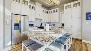 A modern kitchen with white cabinets, a marble island, and a stainless steel refrigerator. - Stunning Lakefront Home With Pickleball, Shared Pool & Sand Volleyball (Kingsland)