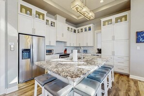 A modern kitchen with white cabinets, a marble island, and a stainless steel refrigerator. - Stunning Lakefront Home With Pickleball, Shared Pool & Sand Volleyball (Kingsland)