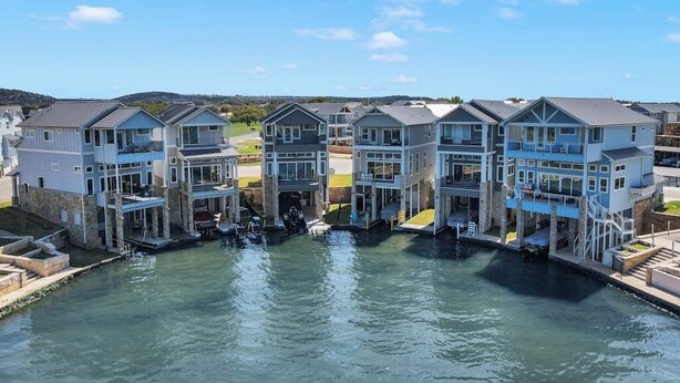 A waterfront property with multiple houses connected by a canal, featuring balconies and outdoor seating areas. - Stunning Lakefront Home With Pickleball, Shared Pool & Sand Volleyball (Kingsland)