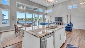 A spacious kitchen with a large island, a dining area with a view, and a living room with a TV and seating. - Stunning Lakefront Home With Pickleball, Shared Pool & Sand Volleyball (Kingsland)