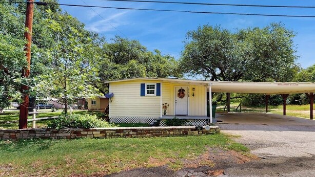 Une petite maison mobile d’un seul étage, dotée d’une véranda et entourée d’arbres, sous un ciel dégagé.