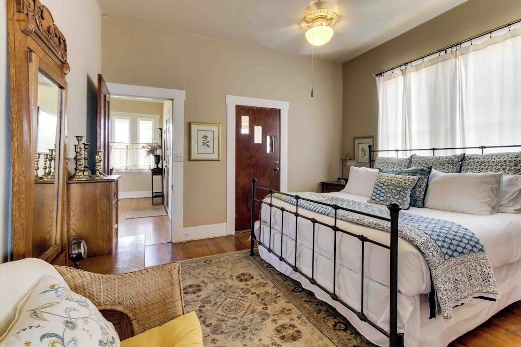 A bedroom with a metal bed frame, a wooden wardrobe, a mirror, and a door leading to another room.