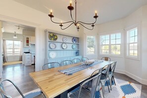 A dining room with a wooden table, metal chairs, a chandelier, and a wall-mounted plate display. - Tranquil Farmstead With Beautiful Views of the Country, Fire pit (Hye)
