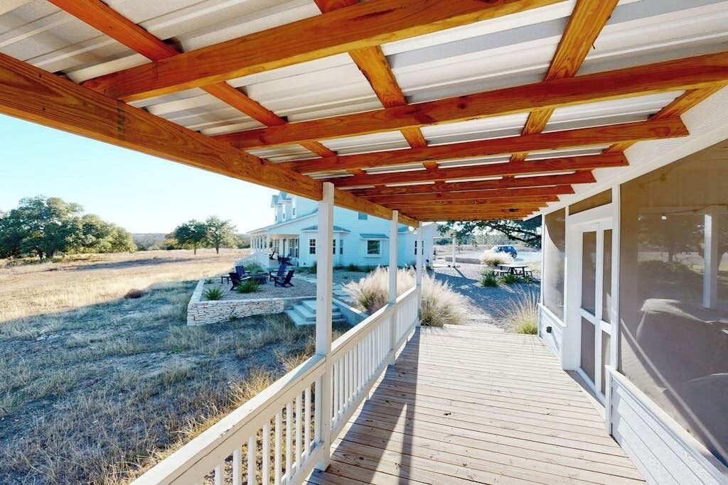 A covered wooden deck leading to a house with a white exterior, a stone pathway, and a grassy yard.