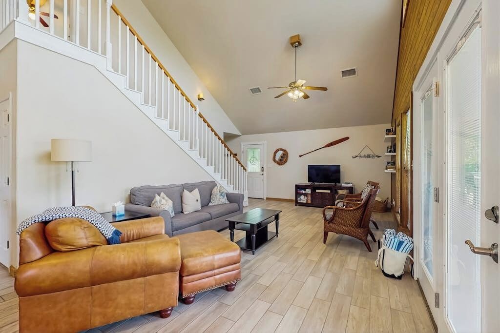 A living room with a sofa, ottoman, coffee table, TV, and a staircase.