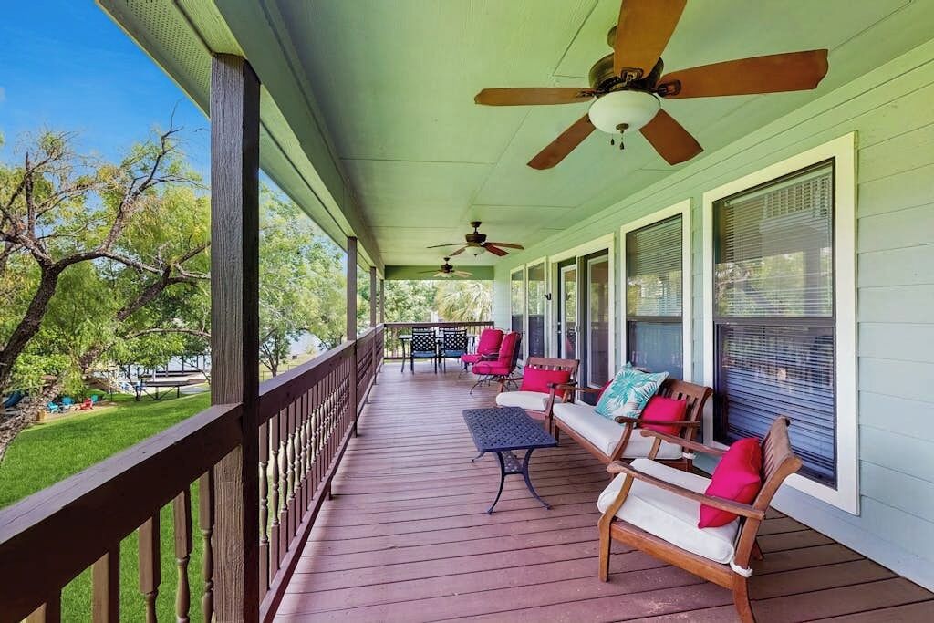 A covered porch with ceiling fans, outdoor seating, and a view of the surrounding greenery.