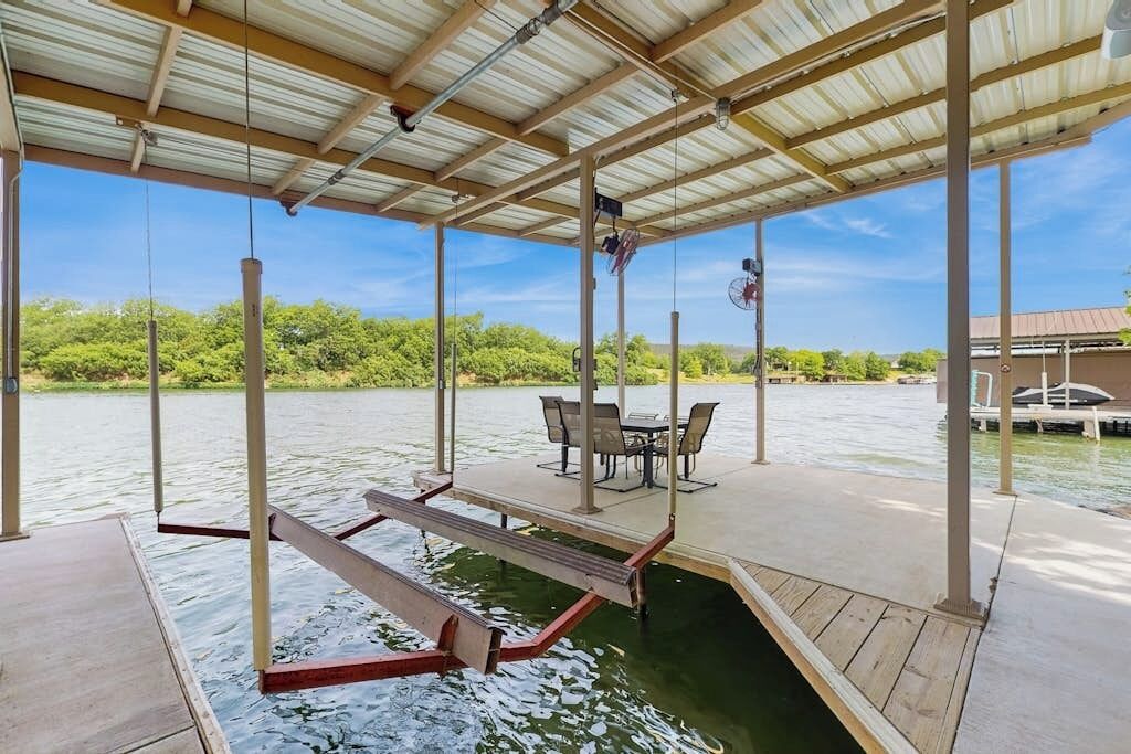 A covered outdoor deck with a table and chairs, overlooking a body of water.