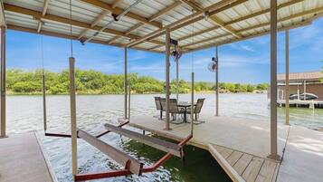A covered outdoor deck with a table and chairs, overlooking a body of water.