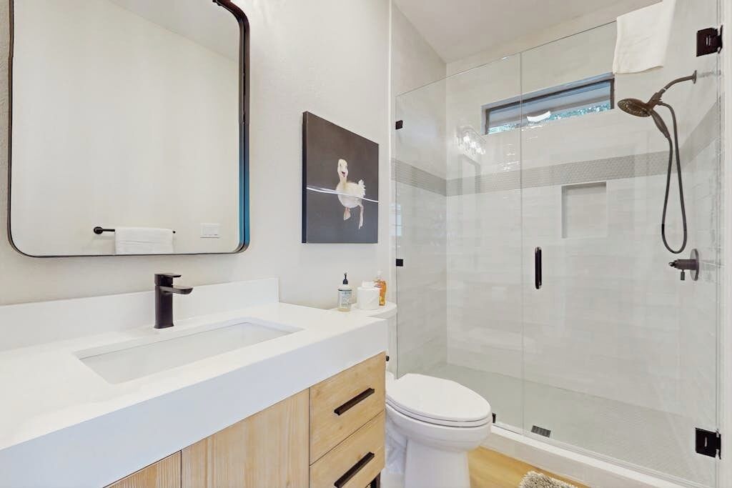 Un baño moderno con un espejo grande, un lavamanos, un inodoro y una ducha con mampara de vidrio.