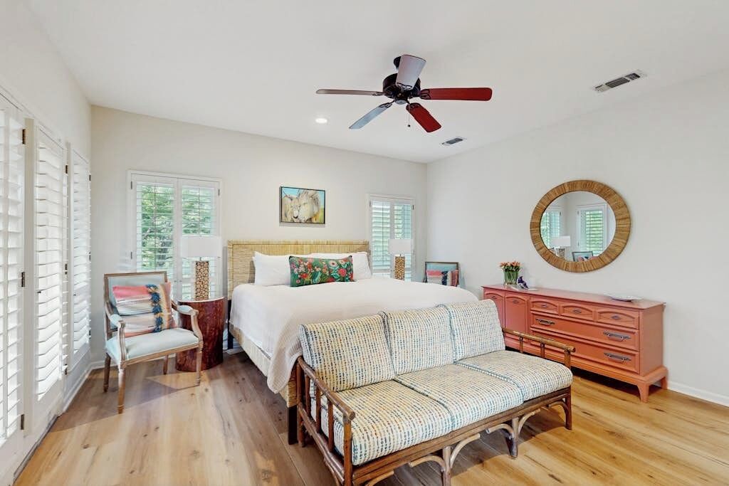 A bedroom with a bed, a chair, a dresser, a round mirror, and a ceiling fan.
