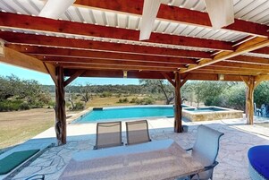 Un espacio al aire libre techado con piscina, piso de piedra y mobiliario.