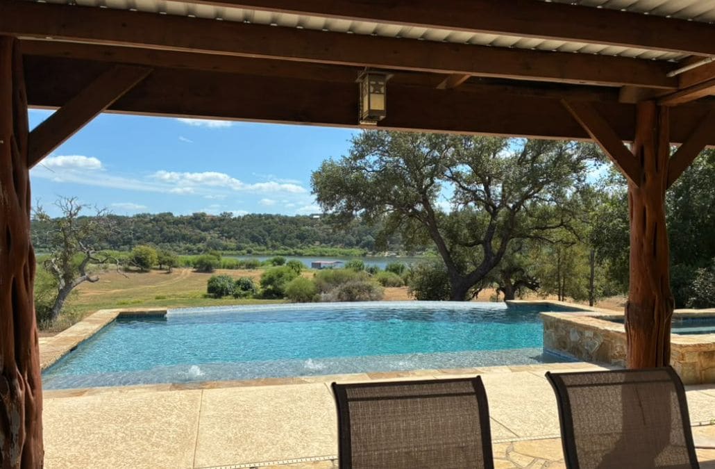 A covered outdoor area with a pool, wooden pergola, and chairs.
