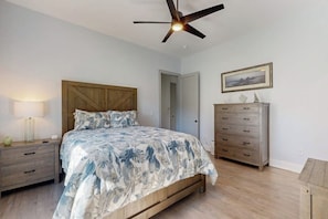 Ein Schlafzimmer mit Bett, Nachttisch, Kommode, Deckenventilator und einem gerahmten Bild an der Wand.