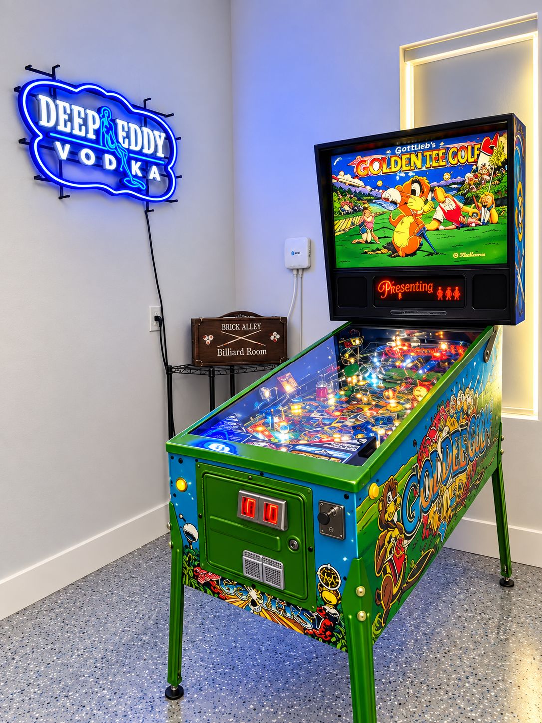 Una máquina de pinball con un letrero de neón para Deep Eddy Vodka y un televisor mostrando Gottlieb's Golden Tee Golf.