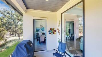A covered patio area with a grill, a dining table, and chairs, leading to an indoor dining space with a glass wall.